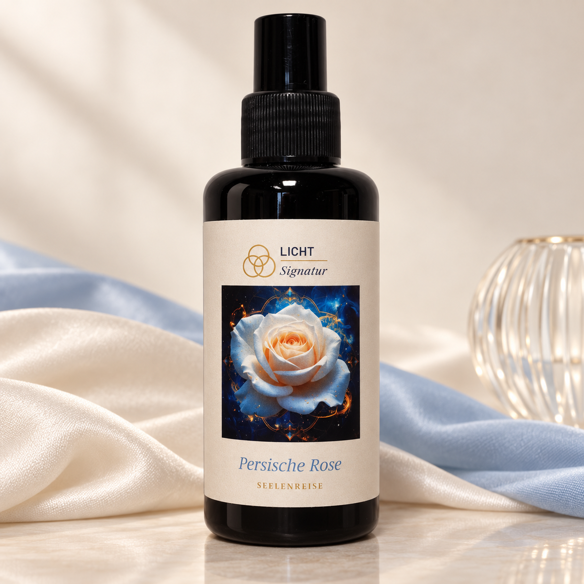 LichtSignatur Persische Rose Spray vor elfenbeinfarbenem und hellblauem Stoff neben einem geriffelten Glasobjekt.